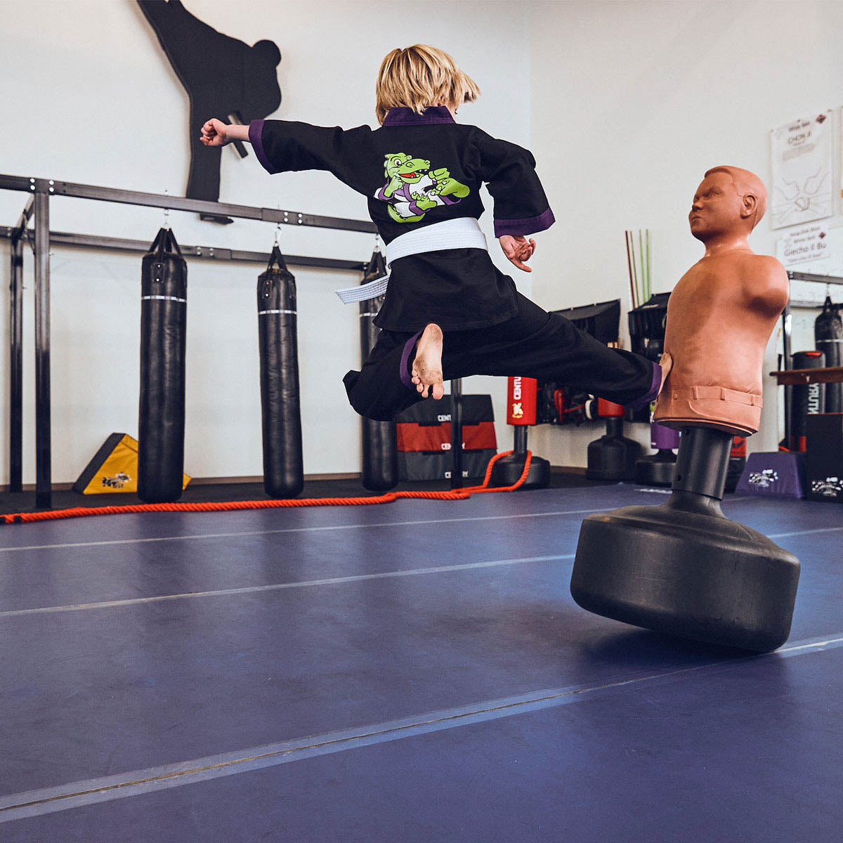 Child wearing black martial arts gi with green dragon back graphic and purple trim
