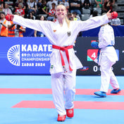 White karate gi with red belt, full-body athlete pose in competition.