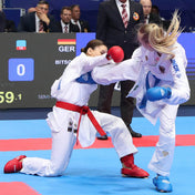 White karate gi with red belt, two athletes grappling on the mat.