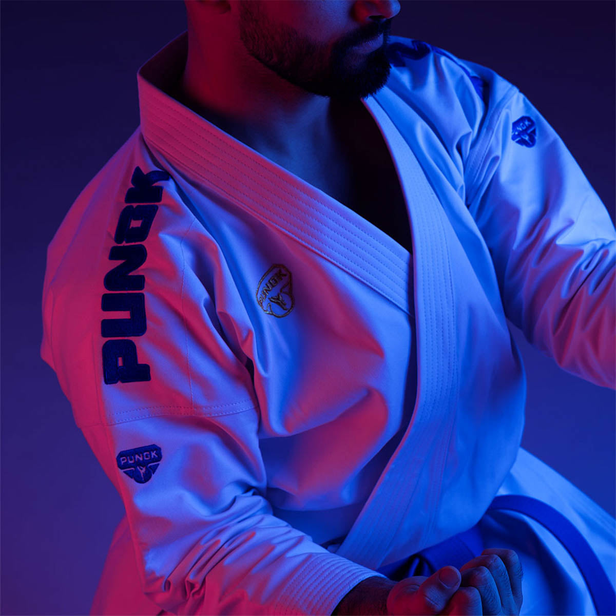 Martial arts gi jacket with woven logo on sleeve, worn with belt and pants