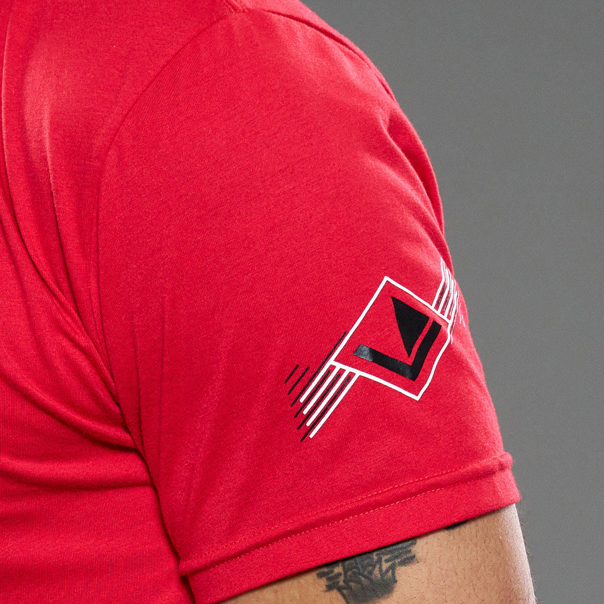 Red unisex t-shirt sleeve with small logo graphic, close-up