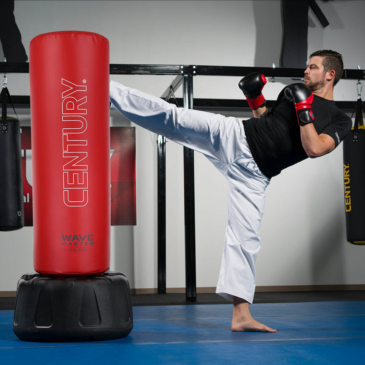 Red Century punching bag with black base, in-use during training kick