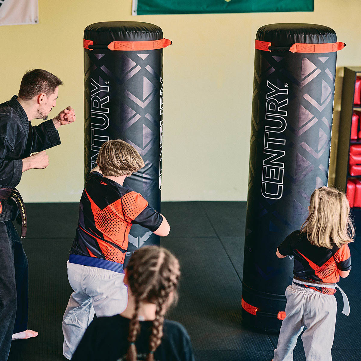 Black freestanding boxing bags with red straps and Century logo panels