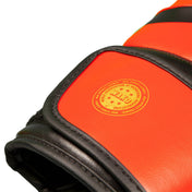 Red kickboxing gloves close-up with round logo patch and black stitched knuckle padding
