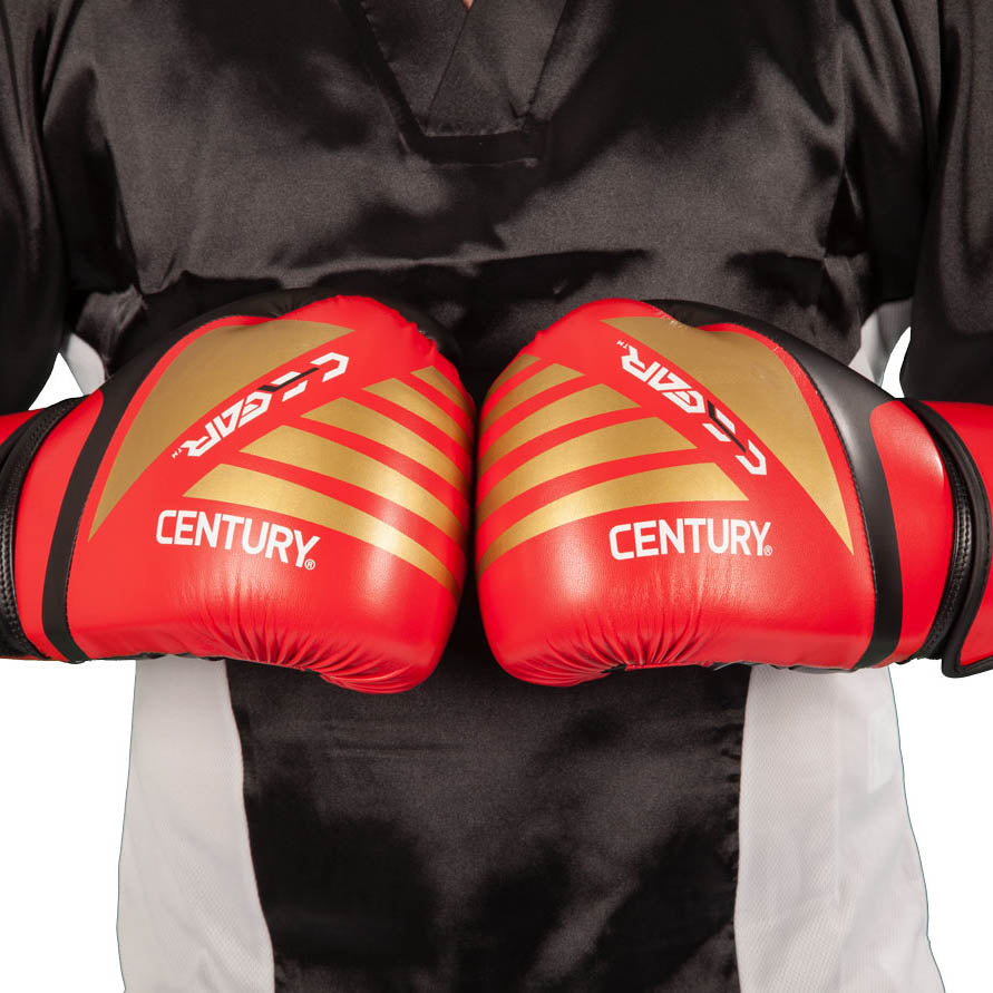 Red kickboxing gloves with gold diagonal stripes and Century branding, pair close-up