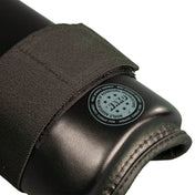Black shin guard with circular stamp on padded knee/shin area and fabric edge stitching.