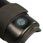 Close-up of black shin guard with circular stamp on padded surface and stitched fabric edge.