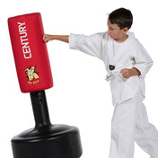 Red kick training pad with cartoon graphic on black freestanding base, held by a child in a gi